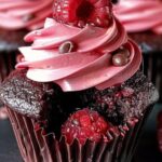 A batch of moist chocolate raspberry cupcakes topped with creamy raspberry buttercream and fresh raspberries.